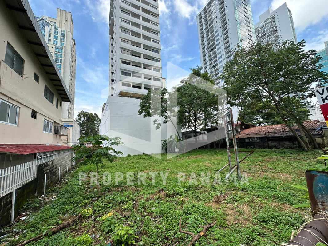 Urban vacant plot with grassy terrain surrounded by towers and advertising signage in Panama City