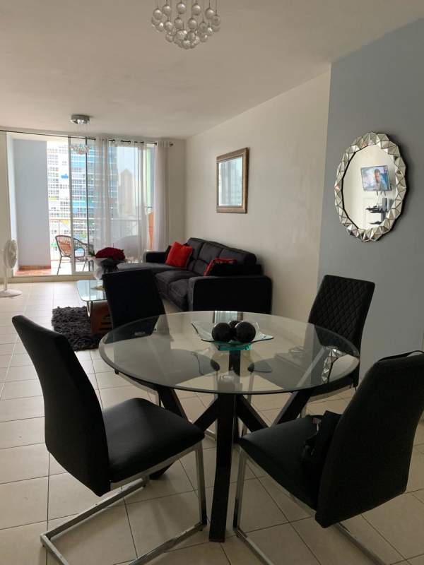 Open-plan living dining area with glass table, black sectional sofa, balcony city view in PH El Cangrejo Plaza Panama