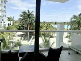 Balcony with glass railing, overlooking palm trees, lagoon and white resort buildings
