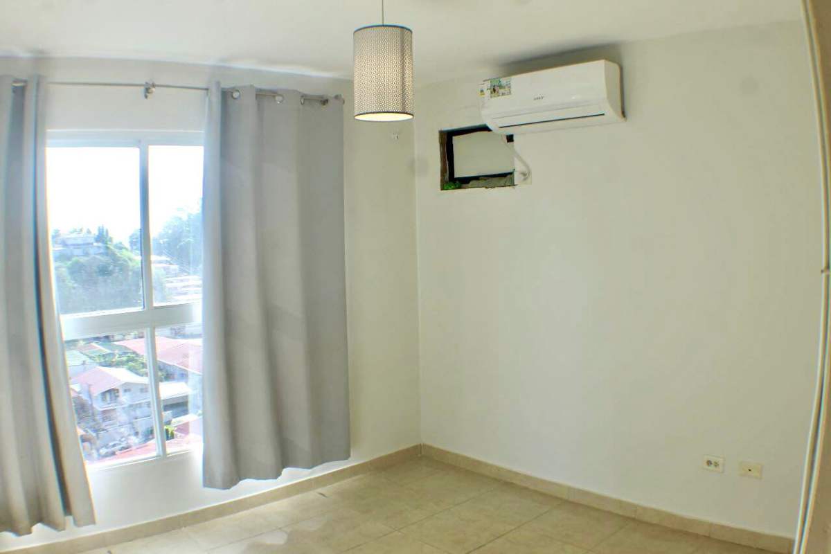 Bedroom with city view window, AC unit, neutral decor in Villa de las Fuentes Panama