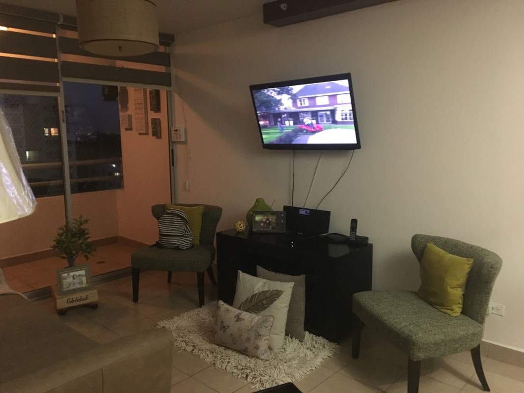 Living room with upholstered chairs, wall-mounted TV and balcony view Parque Lefevre Sky Panama