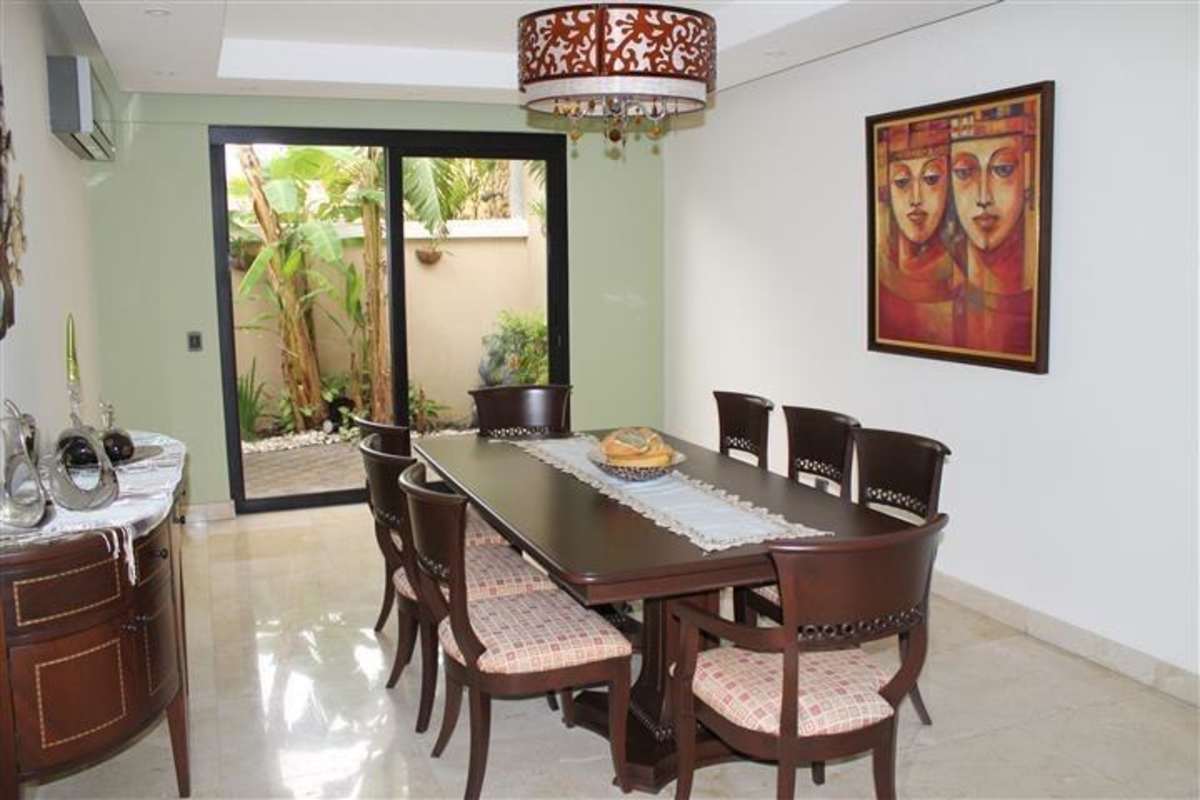 Formal dining room with dark wood table, marble floors, and garden view in Las Perlas villa