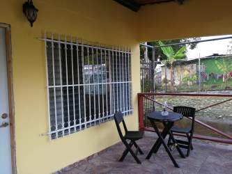 Front facade of yellow Caribbean bungalow house with porch and parking Costa Baja Colon Panama