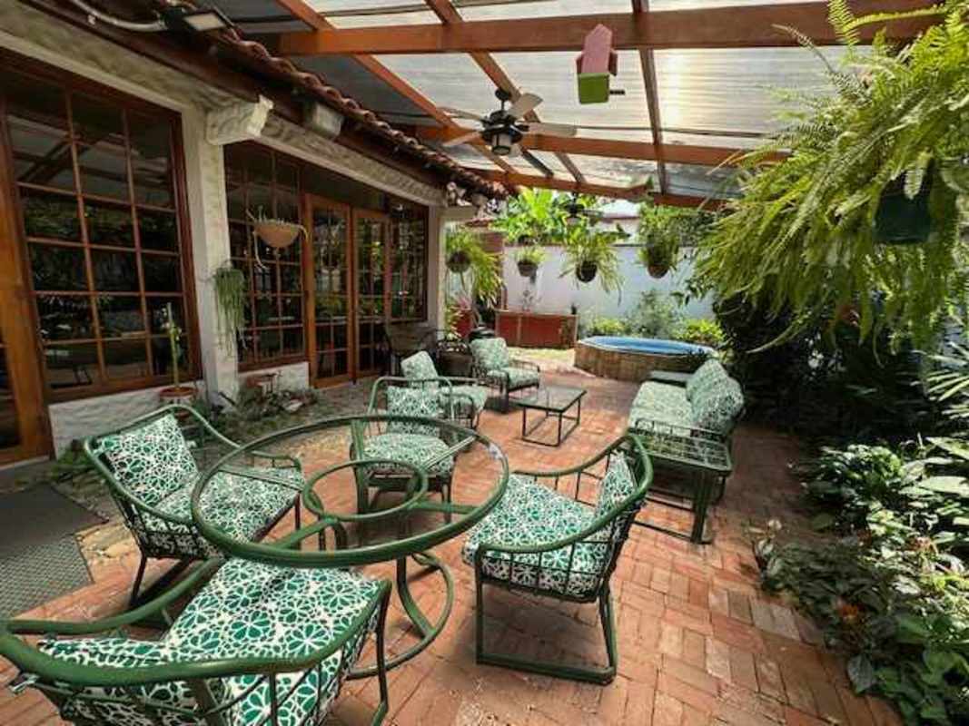 Spacious covered patio with Jacuzzi, barbecue area, rustic furniture, and garden view in La Alameda residence Panama City