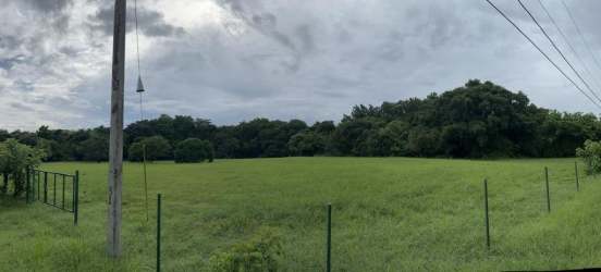 Wide countryside lot with fencing, electric poles, dense trees border and cloudy mountain backdrop in Panama