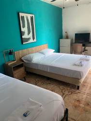 Hotel guest room with two beds, teal accent wall, TV, and ceiling fan in Pedasí Panama