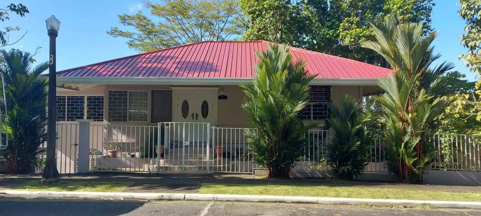 Tropical fenced yard with palm trees covered parking exterior view Clayton Panama home for sale