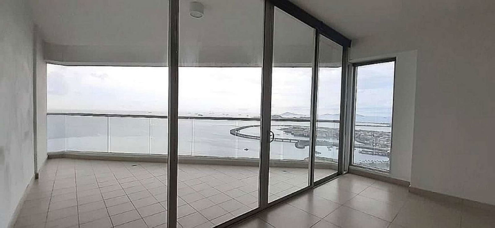 Bedroom with floor-to-ceiling windows showcasing ocean and city skyline in PH Rivage Panama
