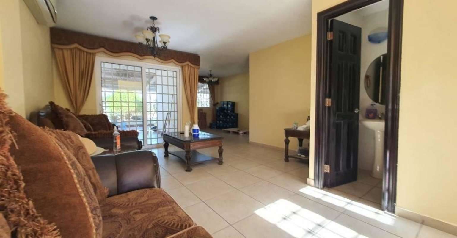 Living area with tile flooring, sofa set, adjacent guest bathroom and large windows in Brisas Heights house Panama City
