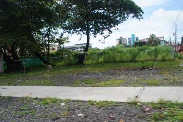 Central Colón vacant lot with grass, trees, adjacent sidewalk and city backdrop Panama