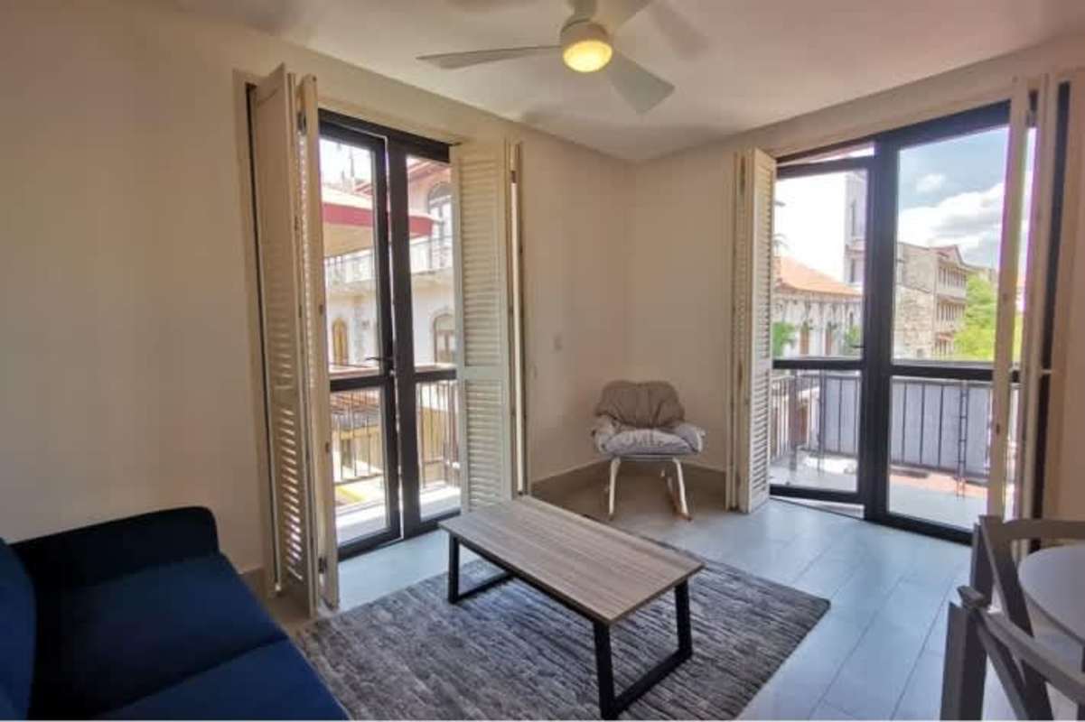 Bright living area with large windows, balcony doors, blue sofa, ceiling fan in PH Casco Viejo San Felipe Panama