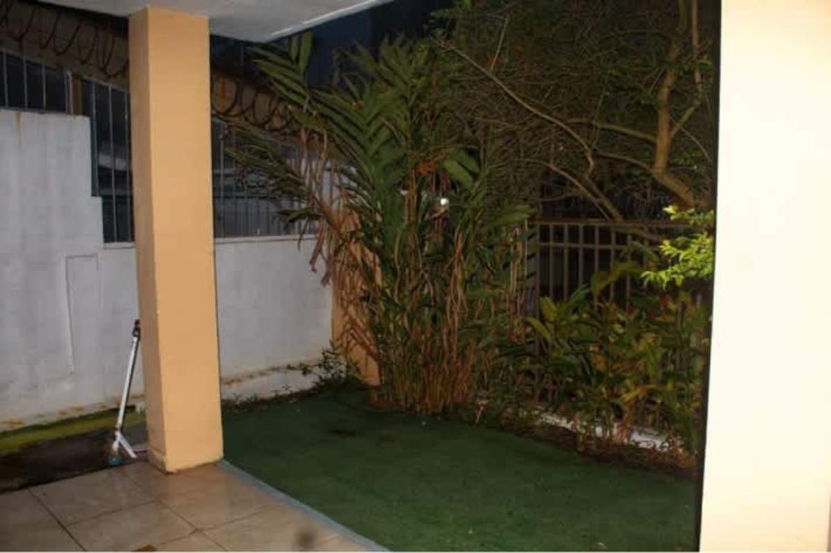 Spacious covered patio opens onto enclosed backyard garden with plants in Betania Panama City