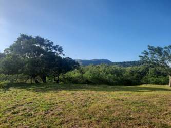Open natural field surrounded by trees and distant hills under clear sky at El Refugio, Penonomé