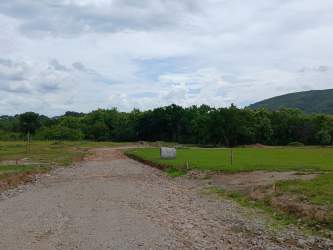 Gravel road passing by lush green open fields with hills in the background at El Refugio Penonomé