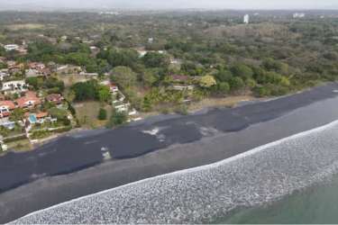 Black sand beach with Pacific Ocean waves and tropical coastal residences in Costa Esmeralda Panama