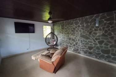 Rustic living room with stone wall, ceiling fan, hanging chair, and TV - commercial house for sale in David Chiriquí
