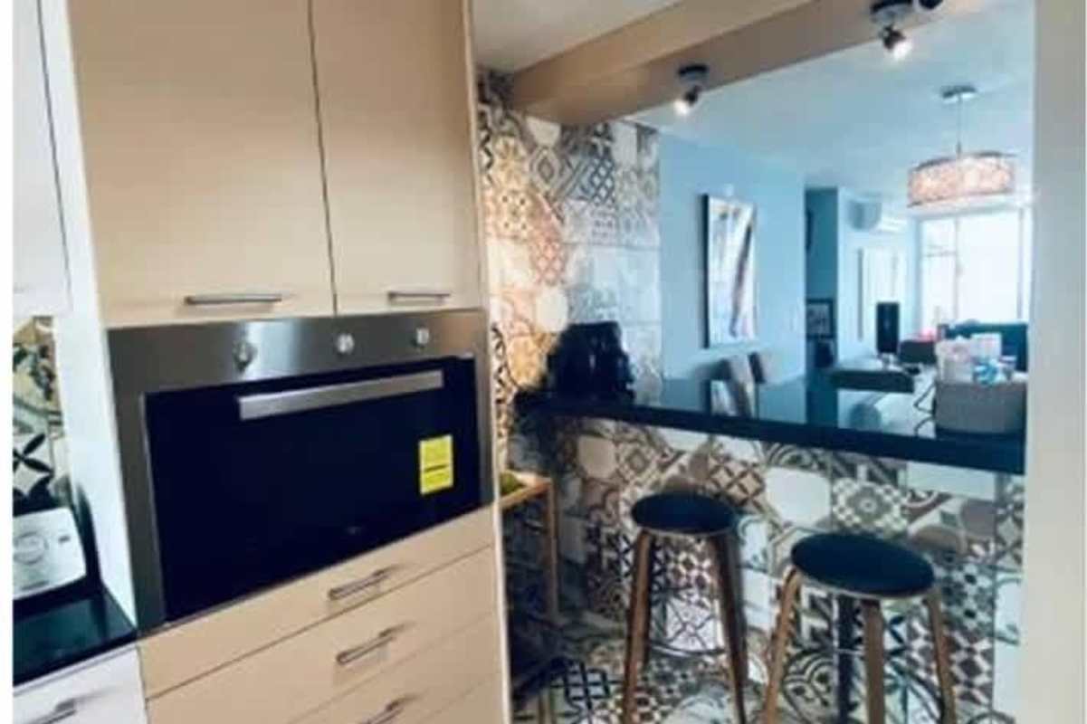 Dining area with wood table, pendant light, artwork and accent wall connected to kitchen in PH The Regent Panama