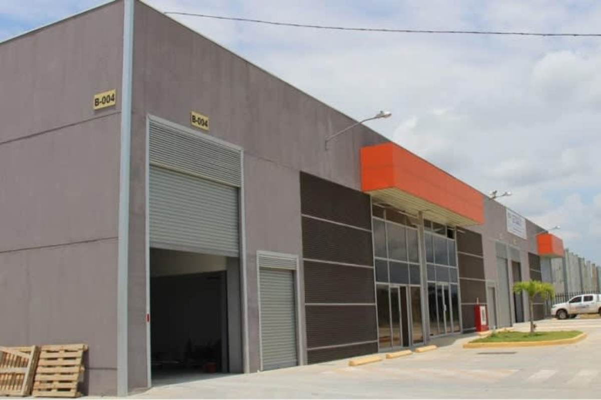 Modern warehouse facade with glass and orange signage, parking in industrial park on Vía Panamericana Panama