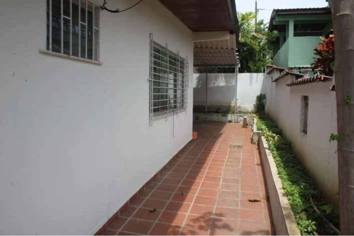 Narrow outdoor walkway along white wall, barred windows, greenery Betania Panama commercial rental