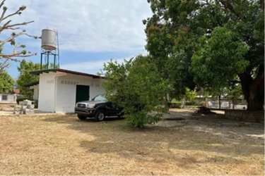 Small white structure with elevated water tank on flat lot with dry yard and trees in Coronado beach area