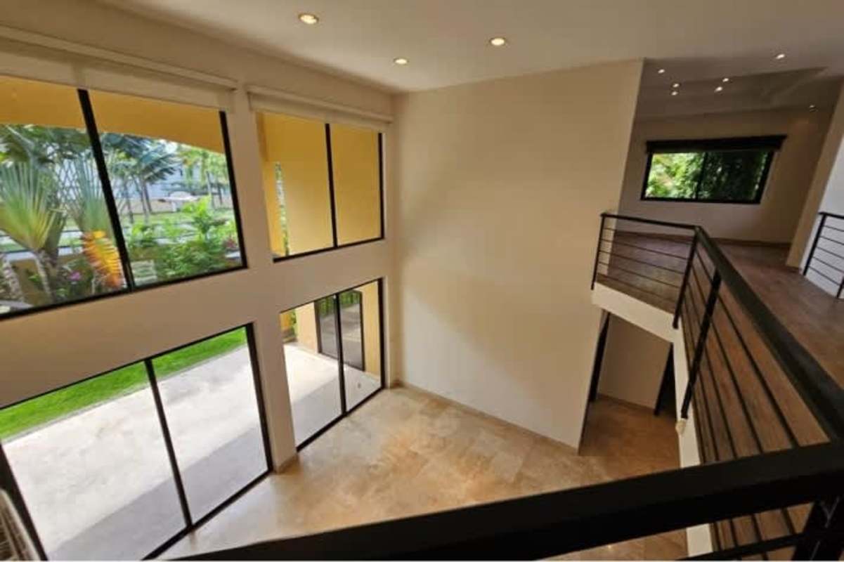 Modern living room with floor-to-ceiling windows, mezzanine balcony, natural light in luxury Antigua Costa del Este home.