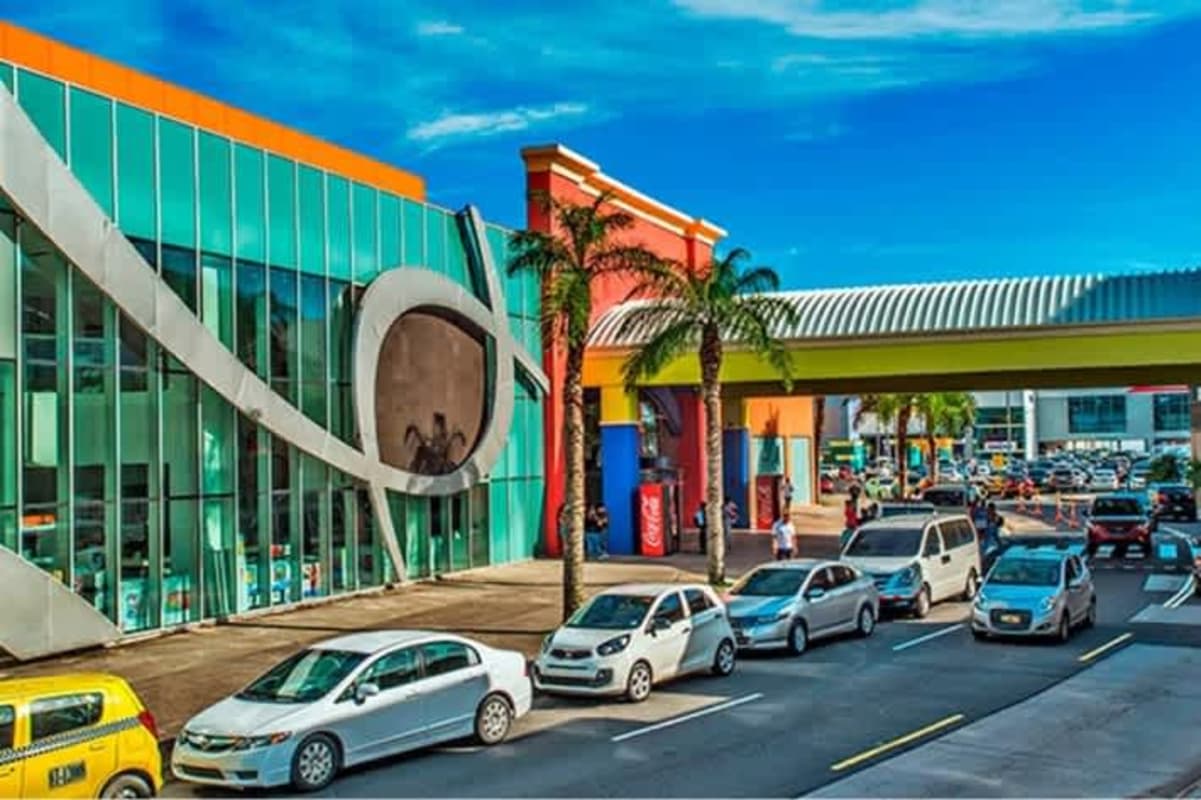 Modern shopping center colorful exterior with glass windows, palm trees, pedestrian bridge Albrook Mall Panama