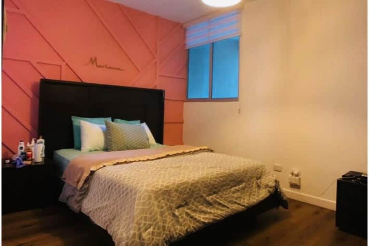 Modern bedroom with peach accent wall, upholstered dark bed, large window blinds PH San Francisco Bay Panama