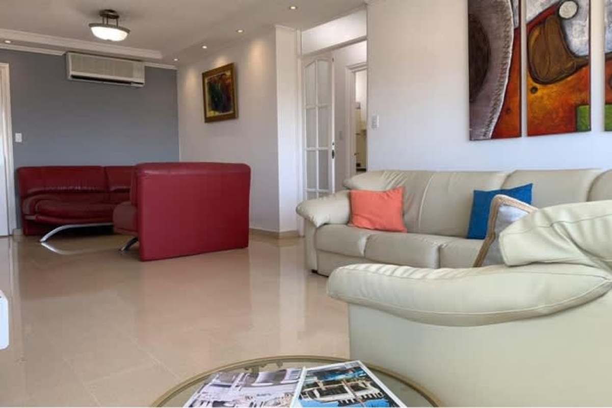 Living room with cream sofa, red armchairs and city views at PH La Alameda Betania Panama City