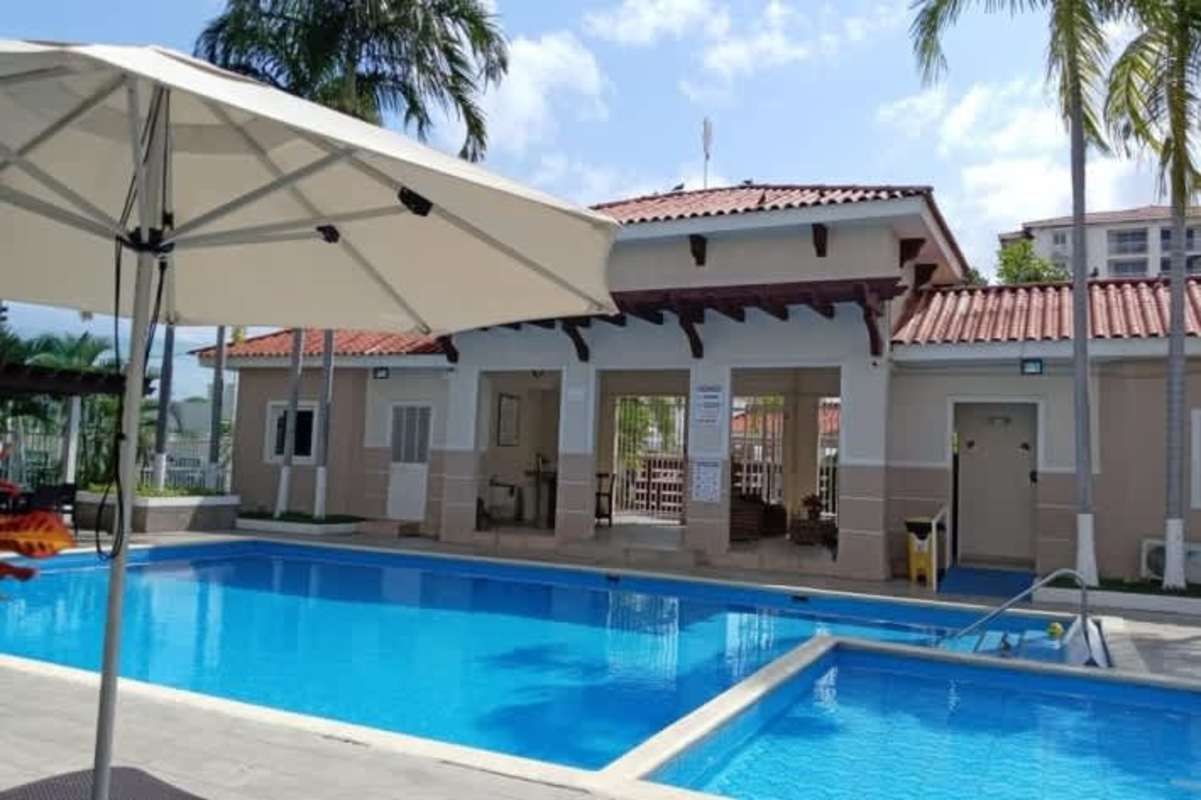 Outdoor swimming pool area with clubhouse and patio umbrellas at Versalles Panama
