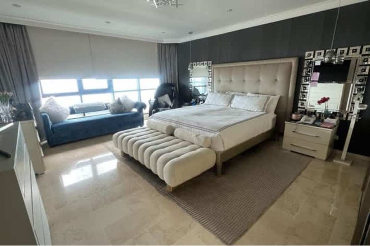 Luxury master bedroom with upholstered headboard, marble floors, and Miami skyline view at PH Miramar Plaza Panama City