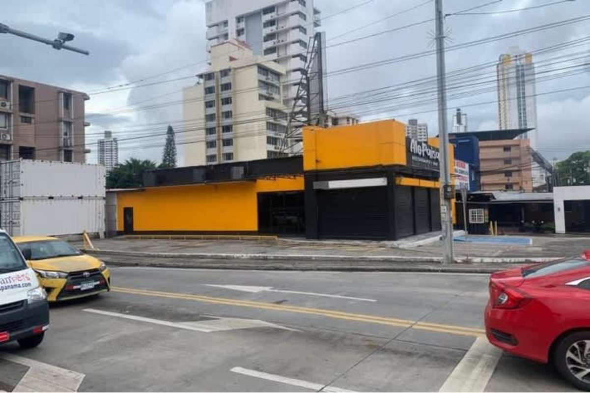 Corner lot with yellow and black commercial units, roll-up shutters, parked vehicles Via España Panama