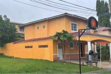 Two-story yellow house with red tiled roof, palms, and fenced yard in Altos de María Leticia Panama