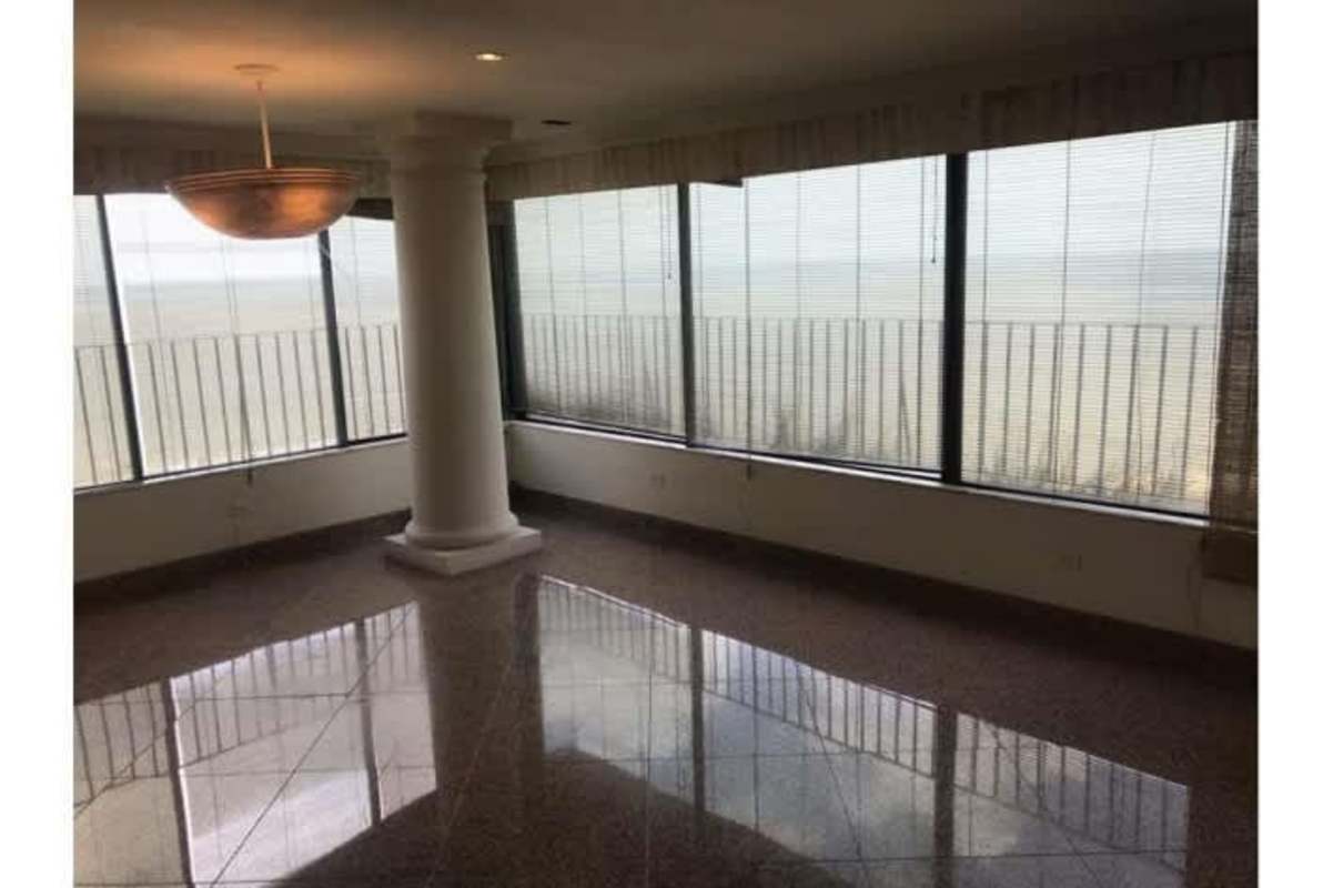 Living room with tall windows, marble floors, and city ocean views in Panama penthouse