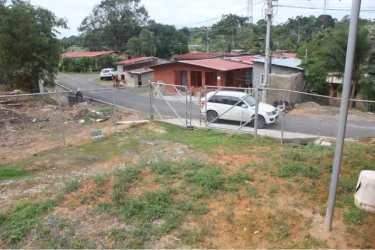 Vacant fenced land along paved street with parked cars in Puerto Pilón Colón