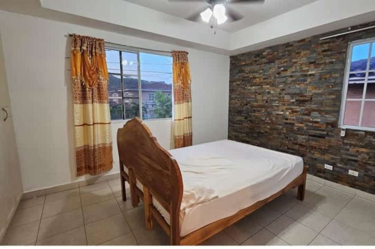 Bedroom with stone accent wall, tile floors, curtains, wood bed in PH Dorado Lakes Panama