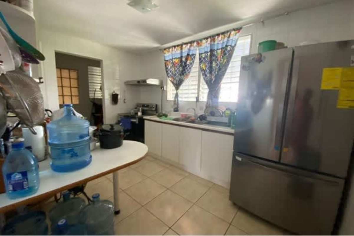 Traditional kitchen with silver refrigerator, gas stove and colorful curtains inside Panama house.