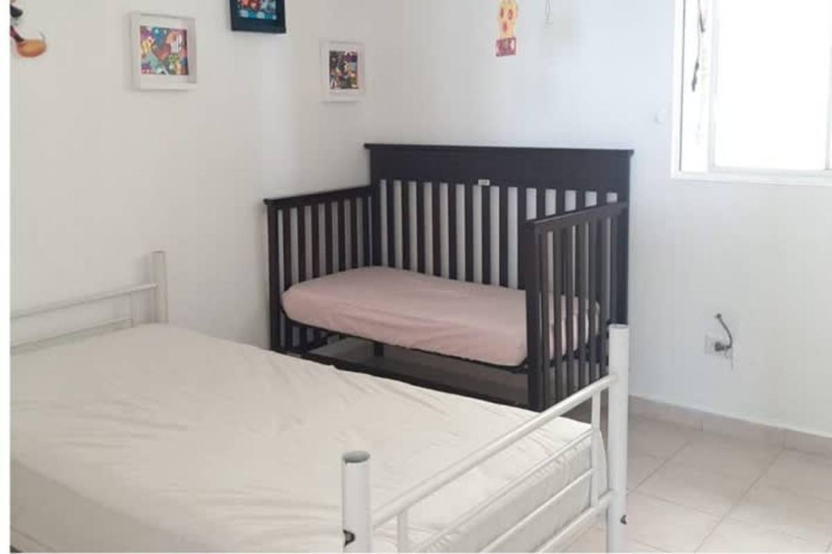 Bedroom with white bed, black crib, window light in budget apartment Juan Díaz Panama