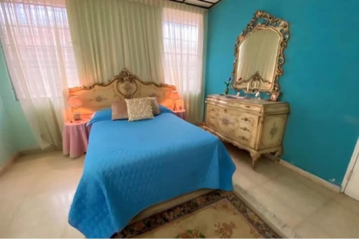 Master bedroom with ornate headboard, vintage dresser, and soft pastel walls in Panama City