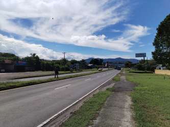 Paved Interamericana road with sidewalk, mountain views, and green areas near Chame property for sale