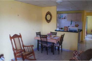 Dining zone with open kitchen, yellow walls, rocking chair and tile floor at house for sale in Urbanización Montelimar, Panama Oeste