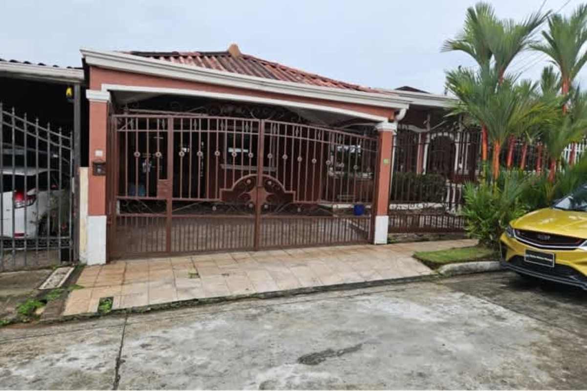 Single family home front view with tiled roof, iron gate, covered driveway and greenery in Altos de Las Praderas San Antonio Panama