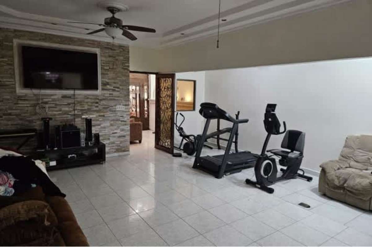 Bright tiled multipurpose living area with ceiling fan, TV accent wall, and space for gym equipment in Altos de Las Praderas Panama