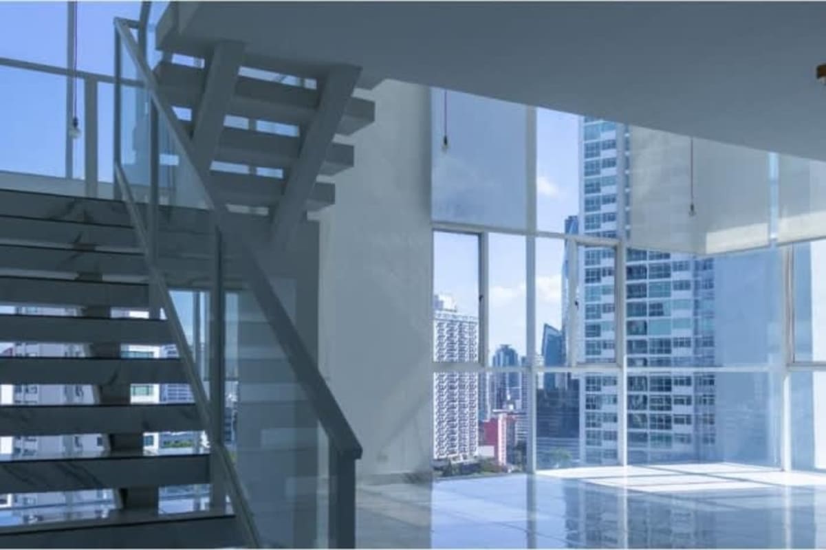 Open plan living and dining loft with glass staircase, large windows, and tile floors at PH Blue Park Bella Vista Panama