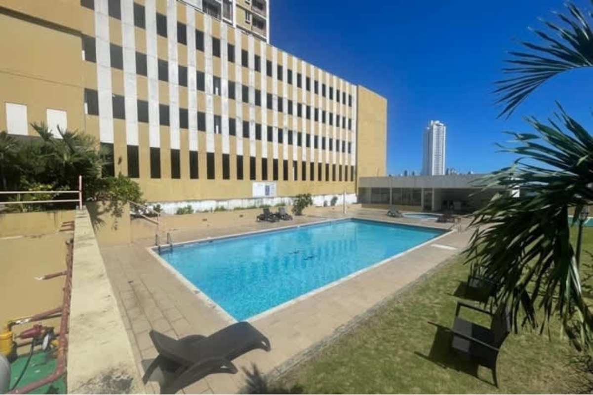 Outdoor swimming pool surrounded by palm trees and urban skyline at PH Avenida Cincuentenario Panama