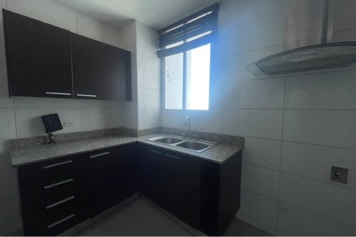 Bright apartment kitchen with granite countertops, dark cabinetry, window, stainless-steel hood in Panama City condo