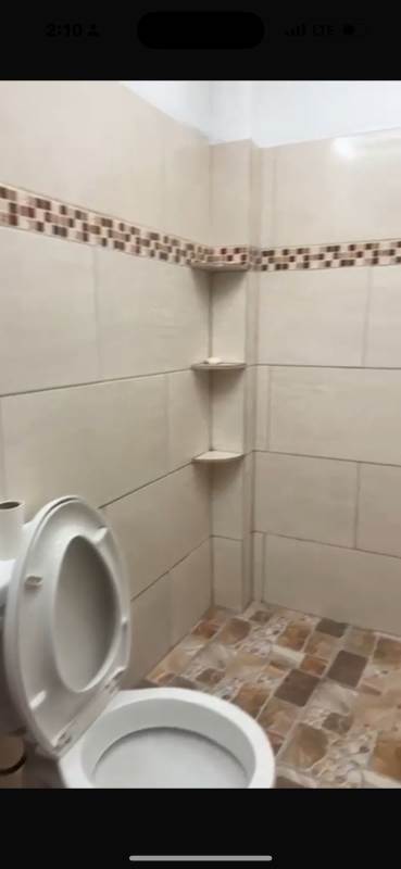 Commercial warehouse bathroom with toilet, beige tiles, accent border, and built-in shelf near Nuevo Tocumen Panama City