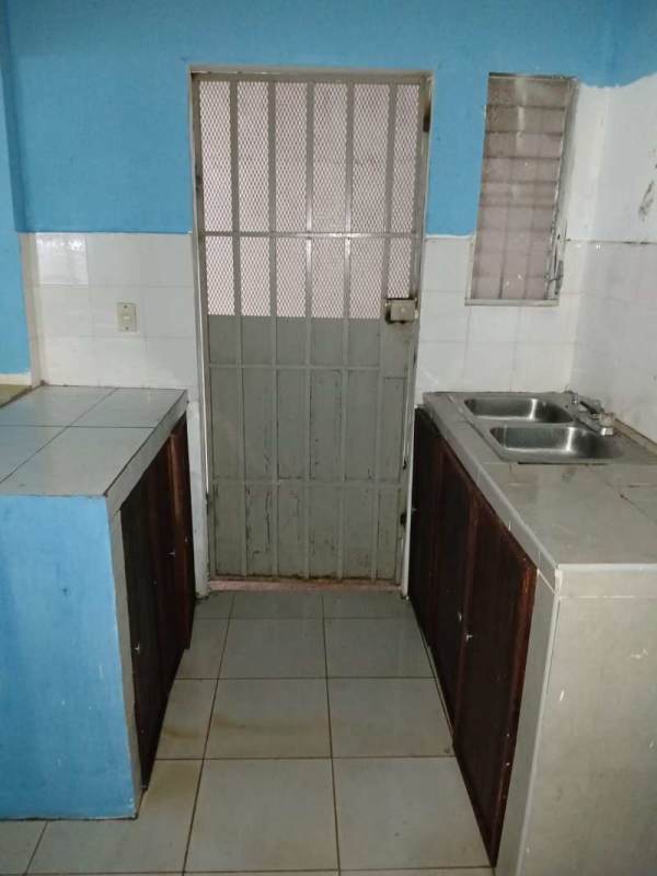 Simple kitchen with blue walls, tiled countertop, double sink and security door in Las Cumbres Panama