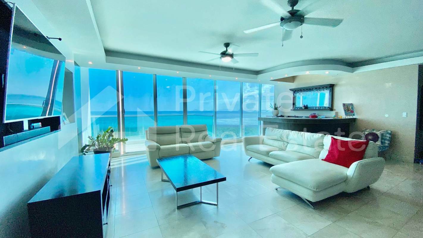 Oceanfront modern living room with large windows, ceiling fans, and balcony access