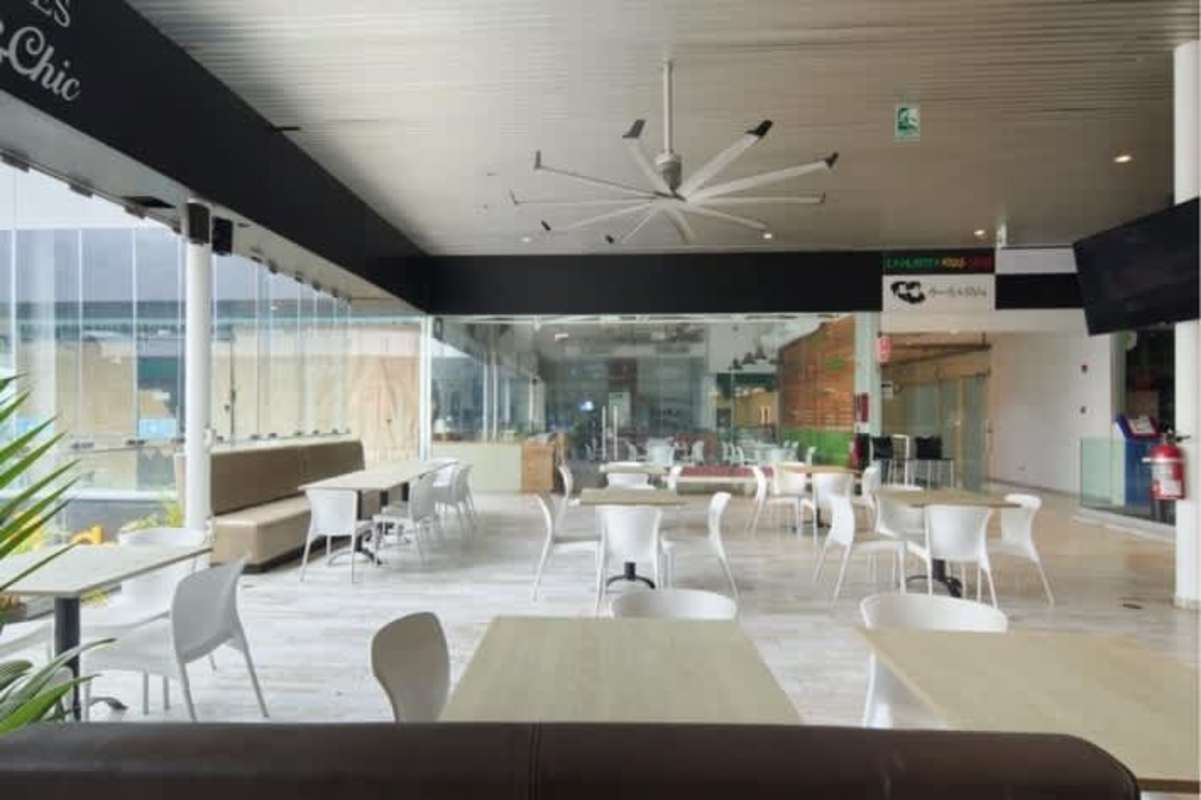Indoor dining court with glass walls, multiple tables, chairs, and large industrial fan at Balboa Boutique Panama City