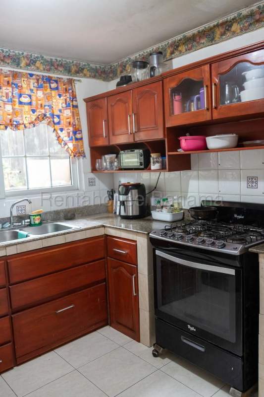 Traditional kitchen with wooden cabinets, granite countertop, double basin sink and decorative curtains in Brisas del Golf Panama